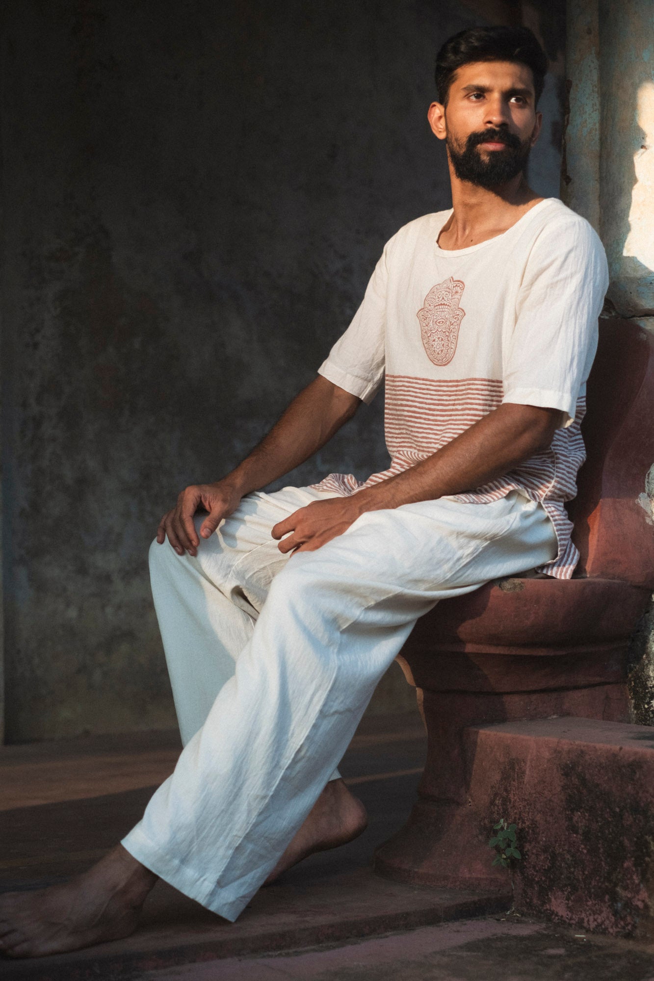 Model seated wearing an organic mulmul cotton kurta with a rust hand motif and striped panel